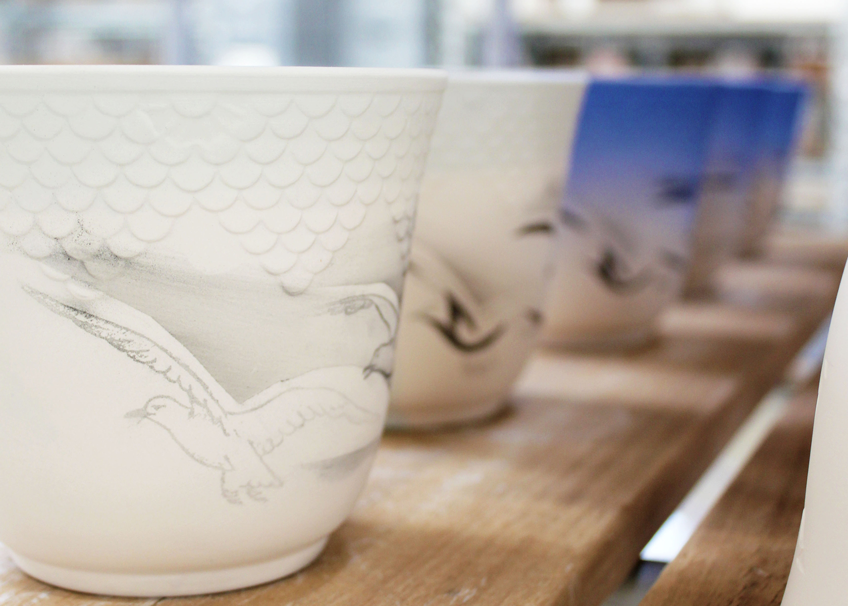 Five Seagull Thermal Mugs on a line where you can see the design process from the first delicate lines to when they have been sprayed with the blue paint